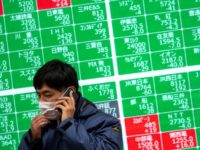 FILE PHOTO: A man wearing a protective face mask, following an outbreak of the coronavirus, talks on his mobile phone in front of a screen showing the Nikkei index outside a brokerage in Tokyo, Japan, February 26, 2020. REUTERS/Athit Perawongmetha